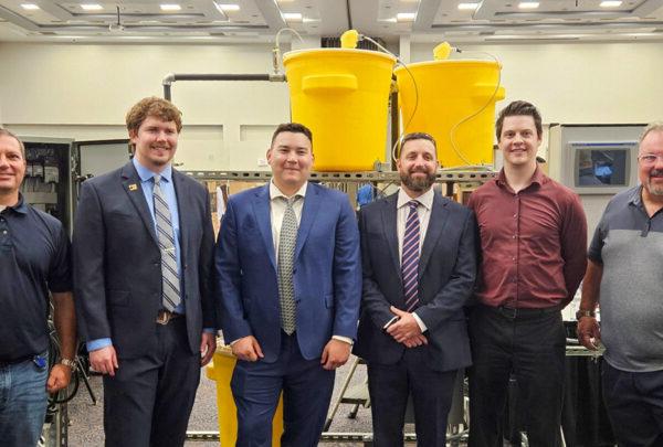 UNF Process Skid 团队成员 pose in front of their senior design project. From left are 格雷格 Kline of Vega Americas; Daniel Fowler, 电; Adrian Hoover, 机械, 布莱斯色鬼, 机械; Lake Miller, 电; 和 澳门足彩app’s Christian Beckman.