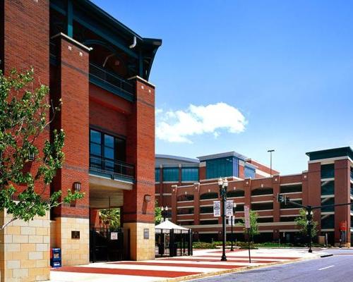 Exterior photo of Jacksonville 市政 Garages. Photo is a view from the street of the sports arena parking garage. 街道两旁都是树木. Red brick with green trim accent the garage.