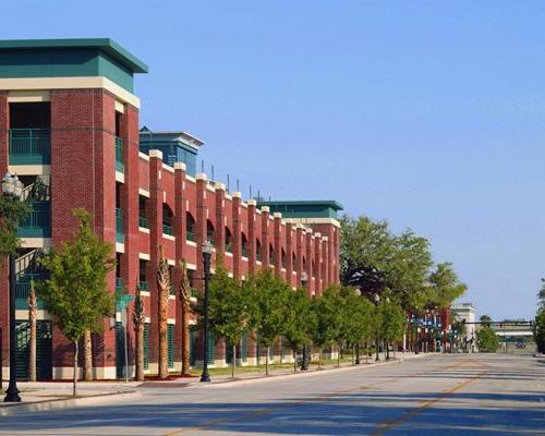 Exterior photo of Jacksonville 市政 Garages. Photo is a streetscape view of the parking garage with a church steeple in the background. 街道两旁都是树木. Red brick with green trim accent the garage.